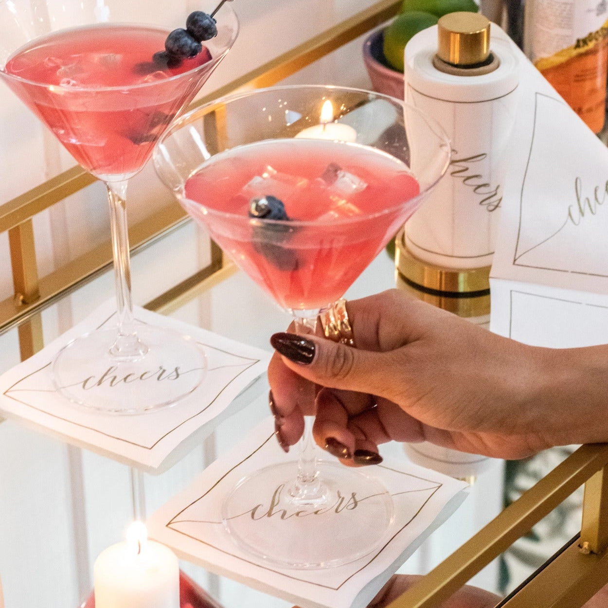 Enhance your bar cart with this gold mini towel stand and roll of white cocktail napkins with gold lettering.