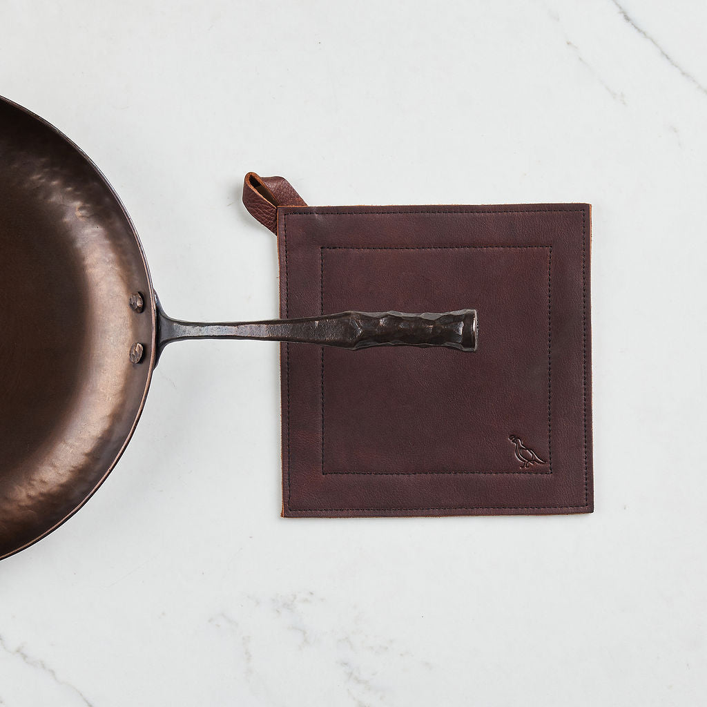 Craftsmanship and performance meet in the Farmhouse carbon steel skillet, shown here with a leather pot holder, sold separately.