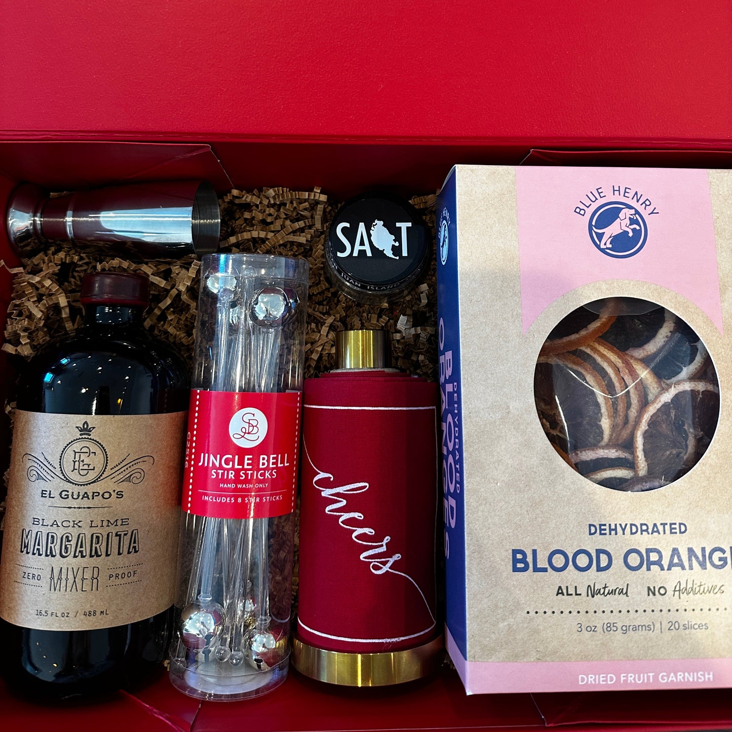 Buy 1 (one) Merry Margarita gift set with black lime margarita mixer, jingle bell stir sticks, gourmet salt, dried blood orange slices, a measuring jigger, and a set of cocktail napkins on a gold stand. 