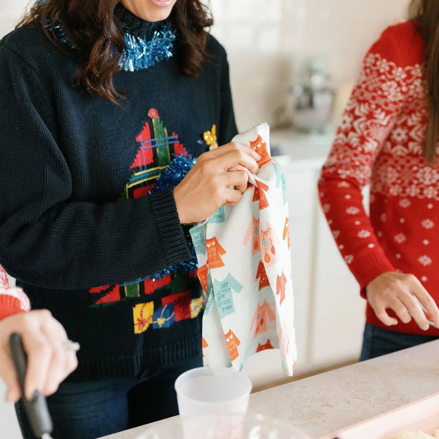 A woman is using the Sweater Weather towel while she and her friends attend an ugly sweater party. Note, the towel print is not ugly.