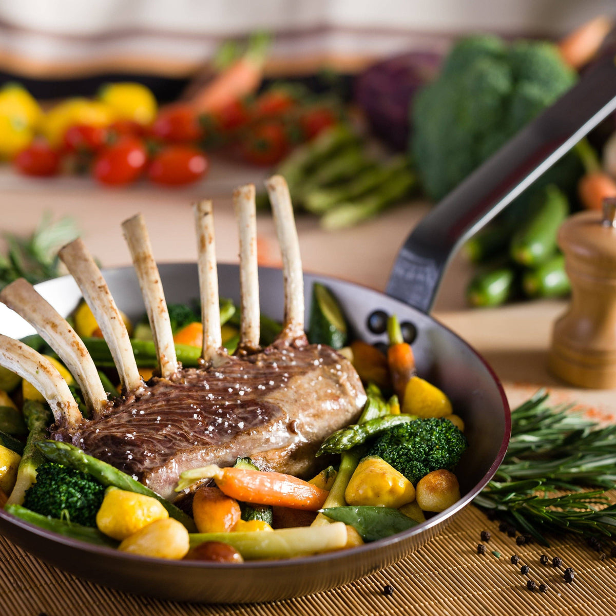 A rack of lamb rests on top of veggies in a de Buyer MINERAL skillet.